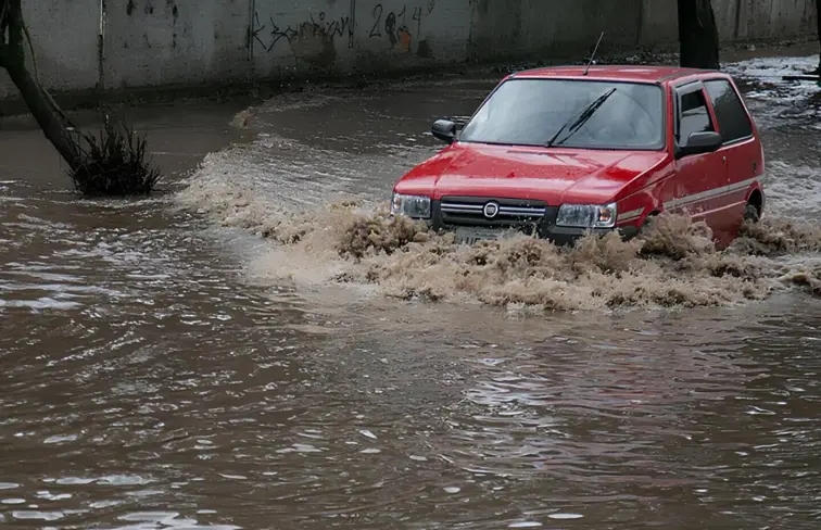 Um carro vermelho a passar no meio de uma estrada inundada